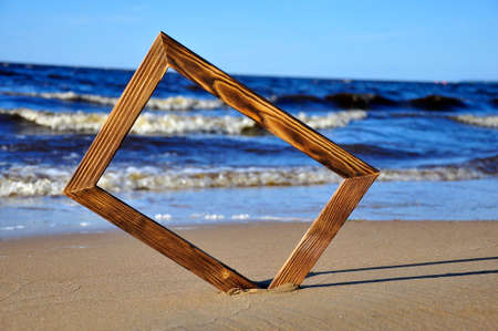 Wooden photo frame on the beach by the sea. Sea surf background.