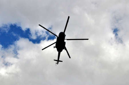 Silhouette of helicopter against blue sky with cloudsの写真素材