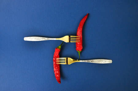 Two gold forks and two red chili peppers on a blue background.