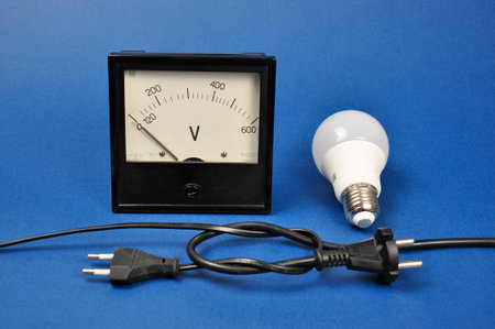 LED lamp and black analog voltmeter on blue background.