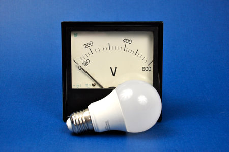 LED lamp and Electro magnetic analog measuring device on blue background. The concept of energy...
