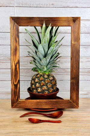 Pineapple in a wooden photo frame against a gray wall.の写真素材