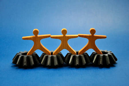 Metal cogs cogwheels and wooden figures of people holding hands.