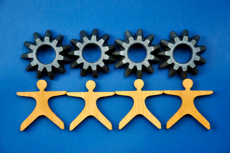 Metal cogs cogwheels and wooden figures of people holding hands.