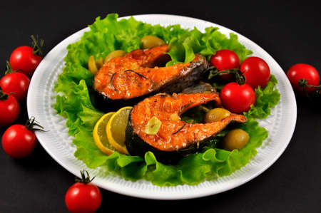 Baked trout on a white plate. Black background.の写真素材