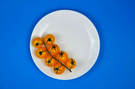 Yellow cherry tomatoes on a white plate. Blue background.の写真素材