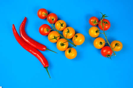 Yellow and red cherry tomatoes and red chilli peppers on a blue background.の写真素材