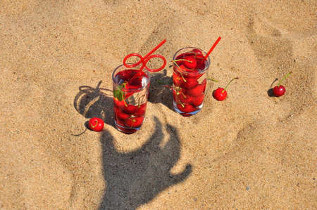 Fresh cherry drink with a straw on a sandy beach.の写真素材