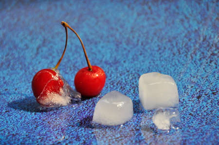 Red ripe cherries and ice on a blue background.