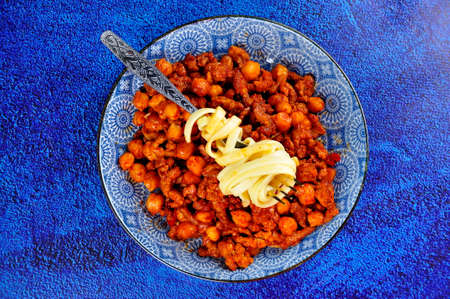 Noodles with meat and chickpeas on a blue plate.の写真素材