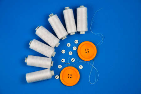 Yellow buttons, needle and coils of thread on a blue background.