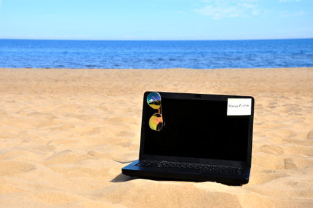 Remote work, a black laptop and sunglasses on a sandy beach.の写真素材