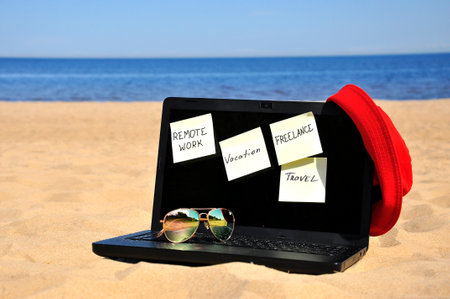 Remote work, a black laptop and sunglasses on a sandy beachの写真素材