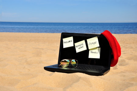 Remote work, a black laptop and sunglasses on a sandy beach.の写真素材