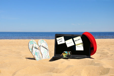 Freelance, a black laptop and sunglasses on a sandy beach.の写真素材