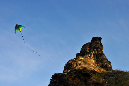 A kite in the blue sky, hovering next to a rock.の写真素材