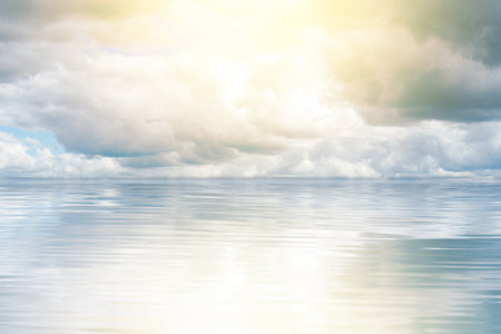 Radiant sun breaking through the clouds, casting a mesmerizing reflection on the tranquil sea.の写真素材