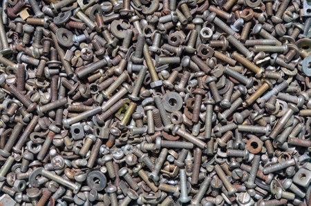Close-up view of a chaotic assortment of various metal washers, screws, nuts, and bolts scattered on a surface, showing different sizes and textures.の写真素材