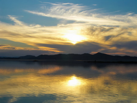 Serene sunset over tranquil lake. Picturesque lake at sunset with vibrant colors reflecting on water, creating a peaceful and serene landscape perfect for backgrounds or wallpapersの写真素材