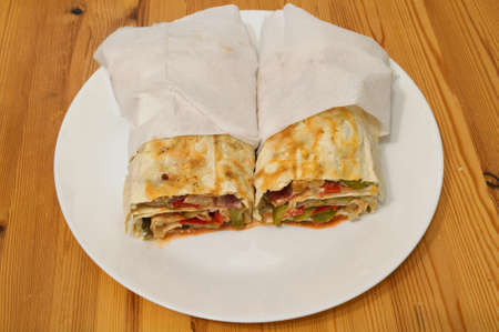 Homemade shawarma in thin wheat tortilla in white plate.