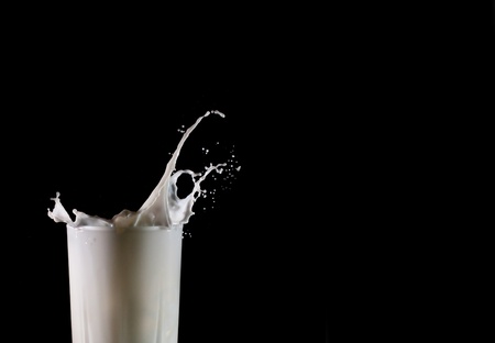 Glass with pouring milk isolated on blackの写真素材