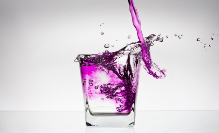 Water splash in a glass with colour water on white backgroung. Pink waterの写真素材