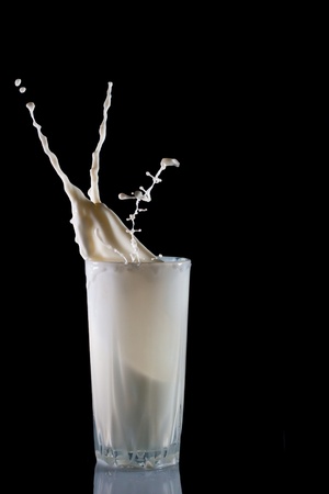 Glass with pouring milk isolated on blackの写真素材