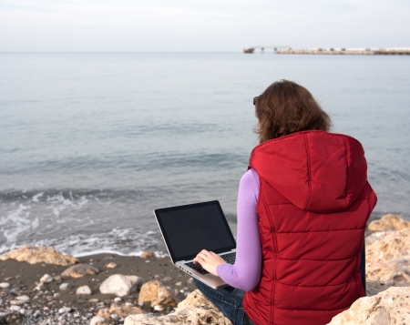 Woman working on the laptop, sitting at the sea coastの写真素材
