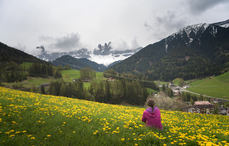 Active young woman-tourist with looking to the Santa Maddalena village in Dolomites. Forested mountains surrounded by green Alpine meadows. The concept of ecological and active tourismの写真素材