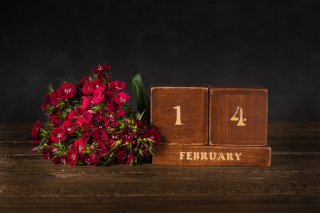 Happy Valentine's Day vintage wooden Perpetual calendar for February 14 on a black background and a bunch of red flowersの写真素材