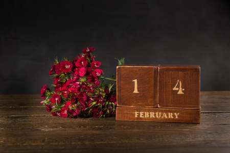 Happy Valentine's Day vintage wooden Perpetual calendar for February 14 on a black background and a bunch of red flowersの写真素材