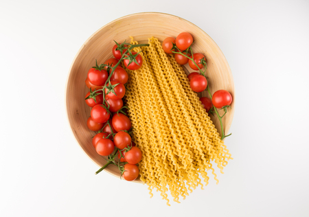 Bowl with raw pasta and tomatoes isolated on white background, top view. Flat layの写真素材