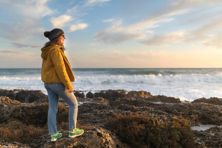Portrait of young woman enjoying sunset near winter sea. Travel Europe in winterの写真素材