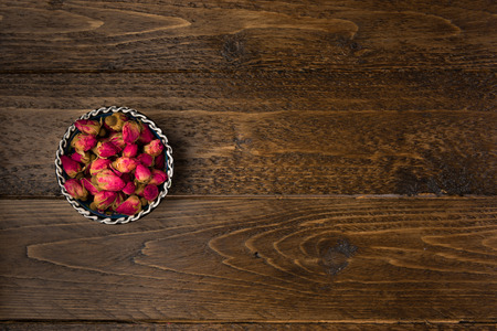 tea rose buds in a clay drinking bowl  isolated on wooden background, top viewの写真素材