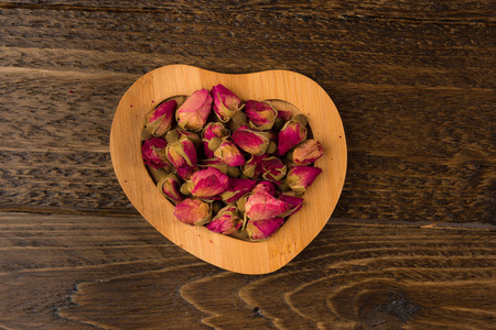 tea rose buds on the wooden saucer  isolated on wooden background, top viewの写真素材