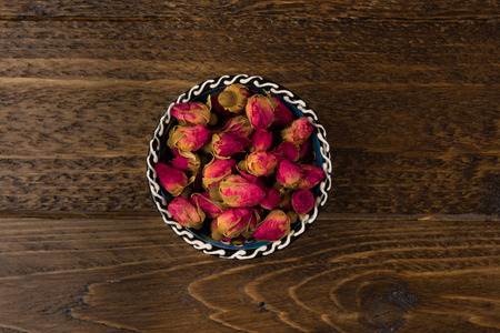 tea rose buds in a clay drinking bowl  isolated on wooden background, top viewの写真素材
