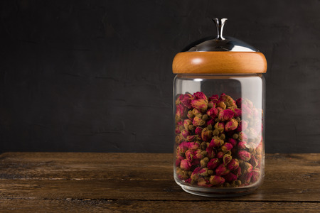 tea rose buds in the transparent jar isolated on the wooden table on black backgroundの写真素材
