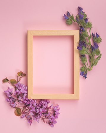 Flowers composition. Purple flowers, leaves and photo frame on pastel pink background. Flat lay, top view, copy spaceの写真素材