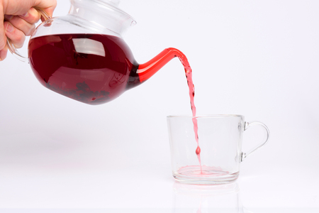 Glass teapot pouring hibiscus tea into cup isolated on white backgroundの写真素材
