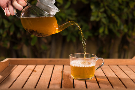 Pouring tea from a teapot into a cup on a blurred background of natureの写真素材