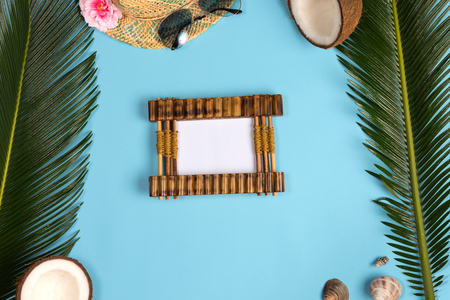 Stylish summer composition with photo frame, green leaves, hat and sunglasses on a blue pastel background. Artwork mockup with copy spaceの写真素材