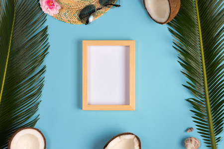Stylish summer composition with photo frame, green leaves, hat and sunglasses on a blue pastel background. Artwork mockup with copy spaceの写真素材