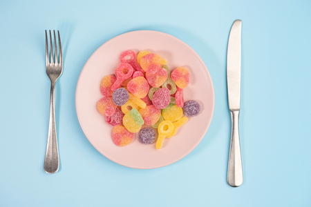Fork, knife and pink plate with gummy candies on blue background.の写真素材