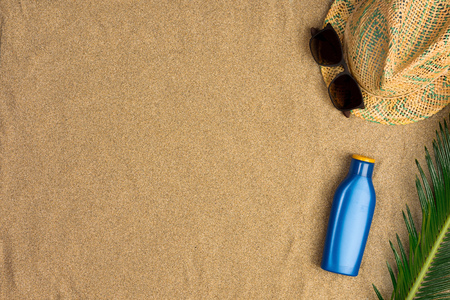 Space for text, beach theme on sand background. Hat, sunglasses, sunscreen on sand background. Top...