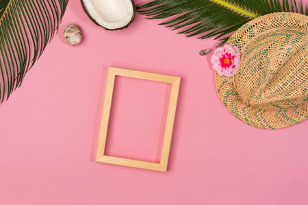 Stylish summer composition with photo frame, green leaves and hat on a pink pastel background. Artwork mockup with copy spaceの写真素材