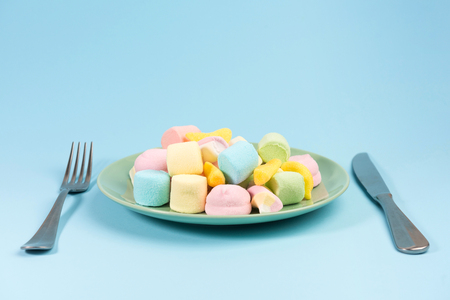 Fork, knife and green plate with marshmallow on blue background.の写真素材