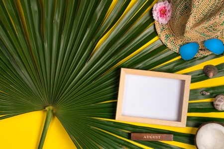 Summer composition with photo frame, green palm leaves, hat and sunglasses on a yellow background. Artwork mockup with copy spaceの写真素材