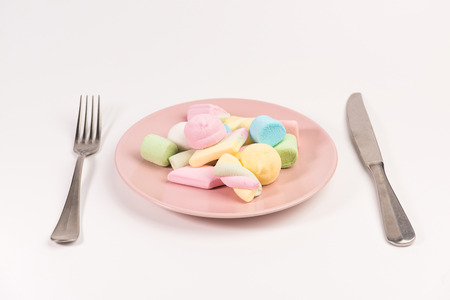 Fork, knife and pink plate with marshmallow isolated on white background.の写真素材
