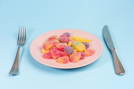 Fork, knife and pink plate with gummy candies isolated on blue backgroundの写真素材