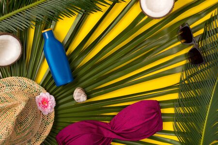 Beach theme on yellow background. Beach accessories and palm leaves on yellow background. Top view.